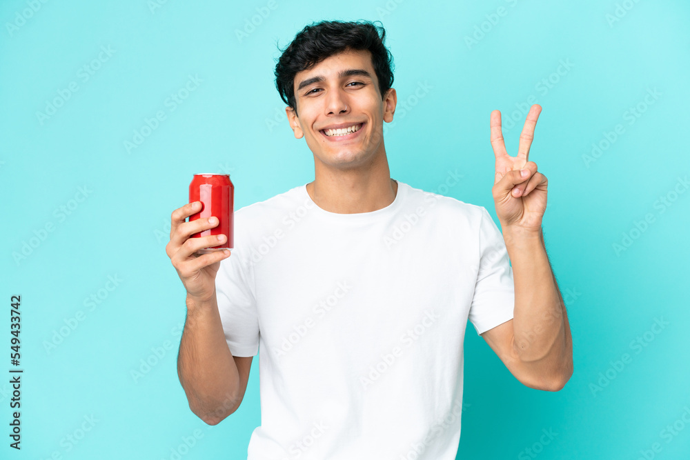 Young Argentinian man holding a refreshment isolated on blue background smiling and showing victory sign Young Argentinian man holding a refreshment isolated on blue background smiling and showing victory sign