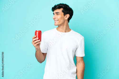 Young Argentinian man holding a refreshment isolated on blue background looking side