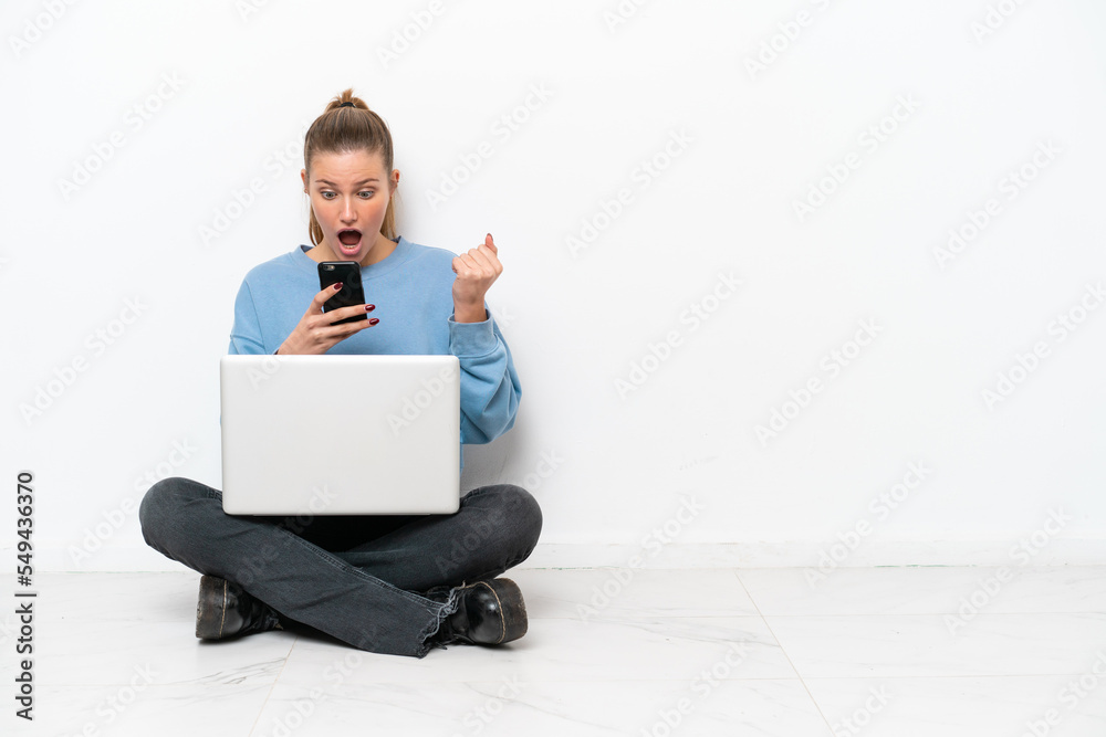Young woman with a laptop sitting on the floor surprised and sending a message Young woman with a laptop sitting on the floor surprised and sending a message