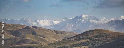 Panorama of a rocky mountain range with snow and glaciers in the evening sunlight in autumn, hills with grass and trees in the foreground