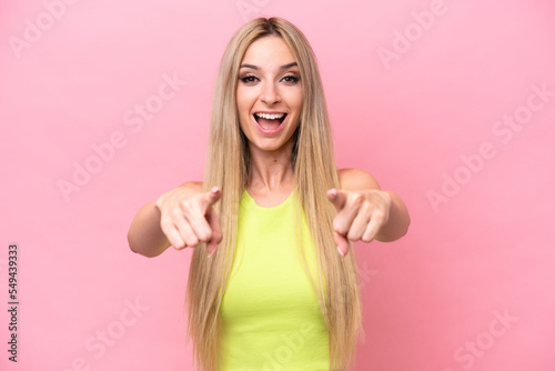 Pretty blonde woman isolated on pink background surprised and pointing front