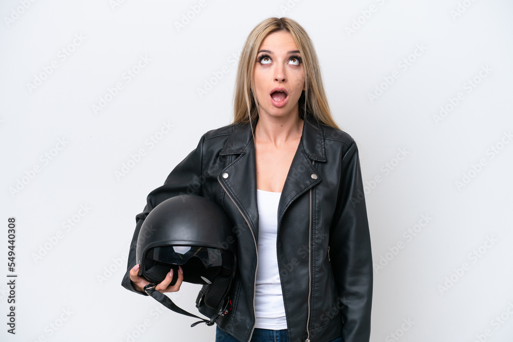 Pretty blonde woman with a motorcycle helmet isolated on white background looking up and with surprised expression Pretty blonde woman with a motorcycle helmet isolated on white background looking up and with surprised expression