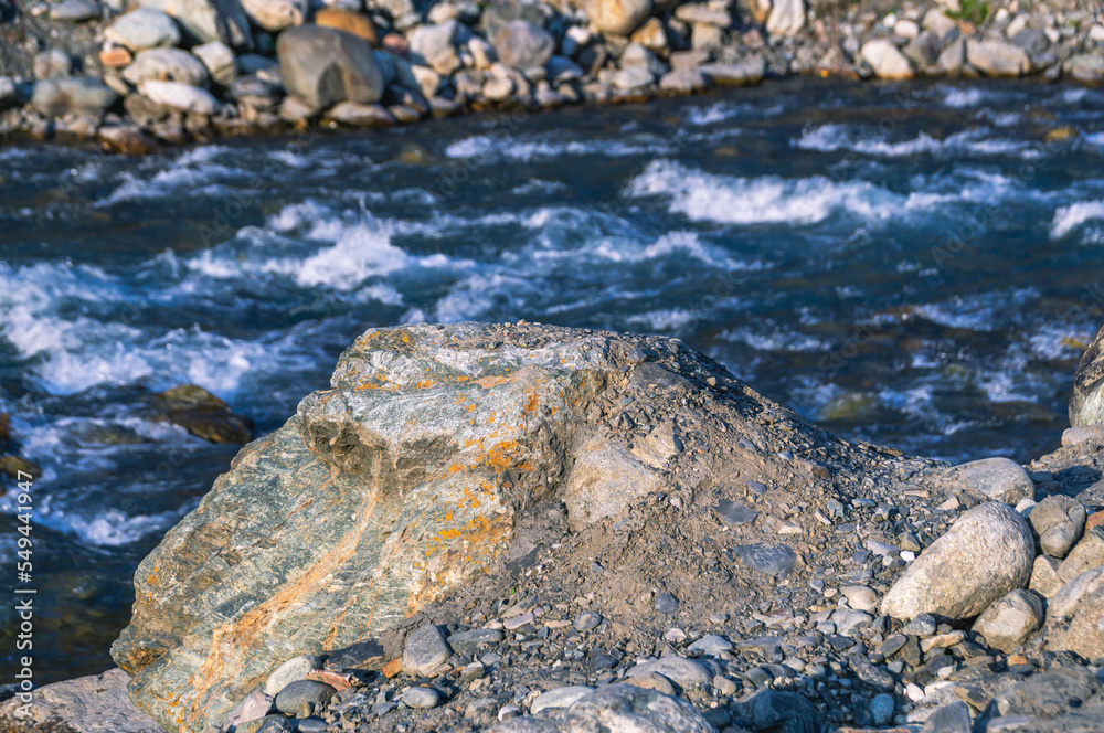 The stone lies near a mountain river. A large rock of solid rock in the mountains. Nature in the mountains.