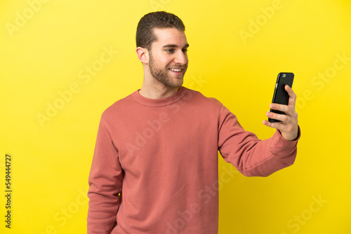 Handsome blonde man over isolated yellow background making a selfie