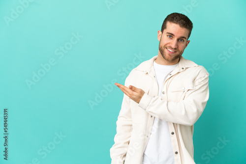Handsome blonde man over isolated blue background presenting an idea while looking smiling towards © luismolinero