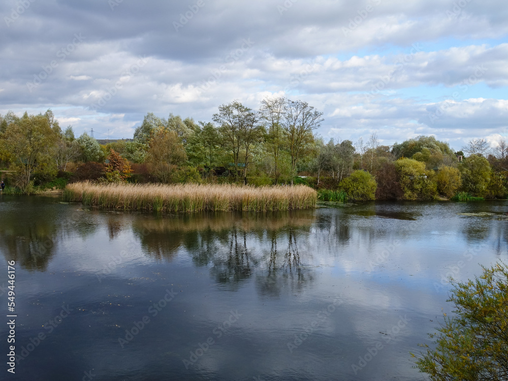 Reflection of sky, gray  rain clouds, and trees in the smooth surface of the lake on an autumn, background