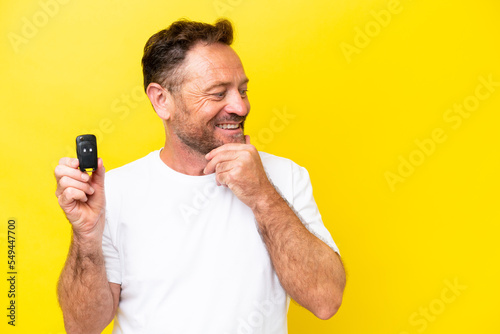 Middle age caucasian man holding car keys isolated on yellow background thinking an idea and looking side