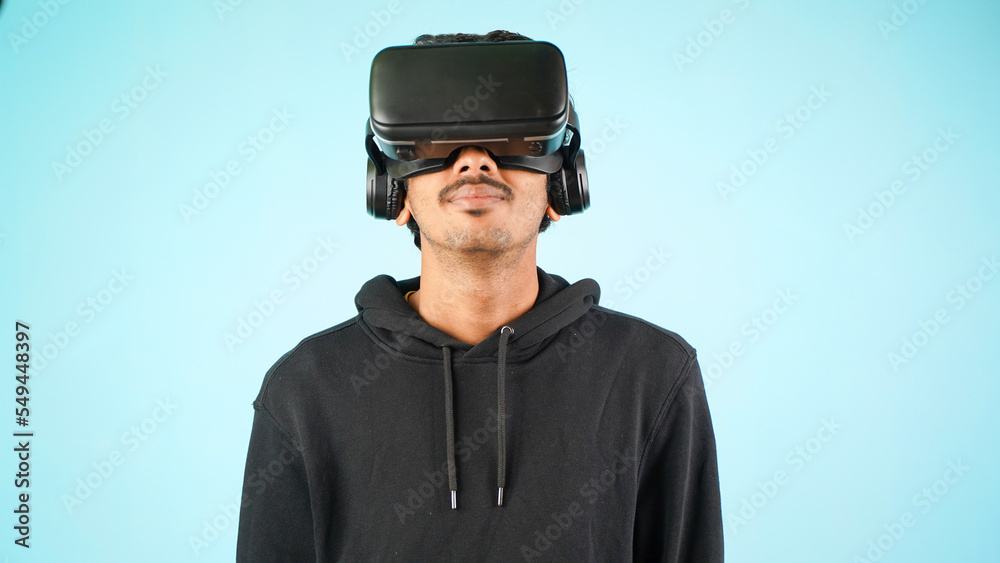 Young Indian Asian man using VR headset, glasses or goggles, isolated over blue colour indoor studio background, future, gadgets, technology, education online, studying, video game concept Young Indian Asian man using VR headset, glasses or goggles, isolated over blue colour indoor studio background, future, gadgets, technology, education online, studying, video game concept