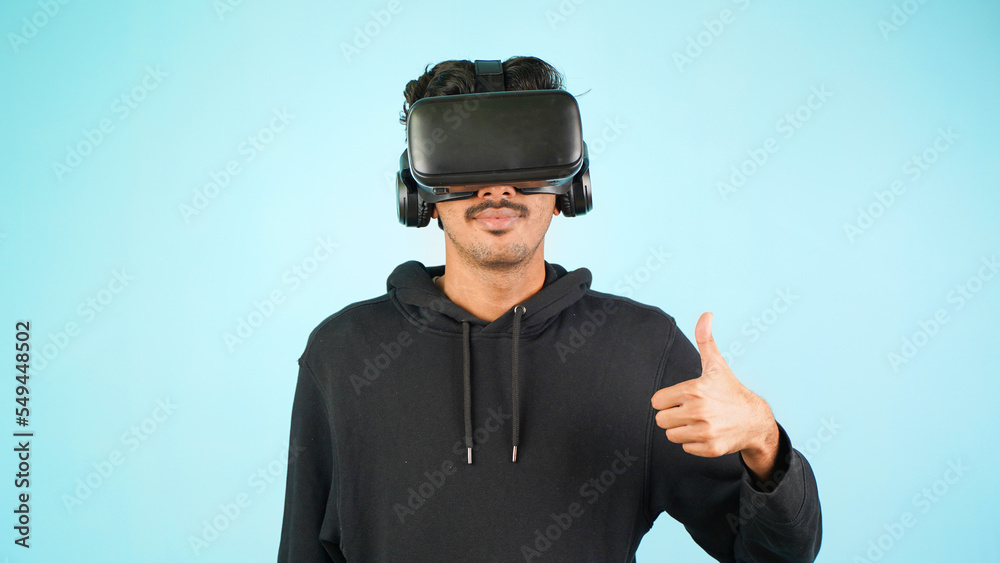 Young Indian Asian man using VR headset, glasses or goggles, isolated over blue colour indoor studio background, saying nice gesture, happy or happiness Young Indian Asian man using VR headset, glasses or goggles, isolated over blue colour indoor studio background, saying nice gesture, happy or happiness
