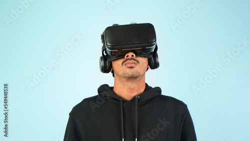 Young Indian Asian man using VR headset, glasses or goggles, isolated over blue colour indoor studio background, future, gadgets, technology, education online, studying, video game concept © Arnav Pratap Singh