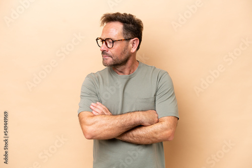 Middle age caucasian man isolated on beige background keeping the arms crossed
