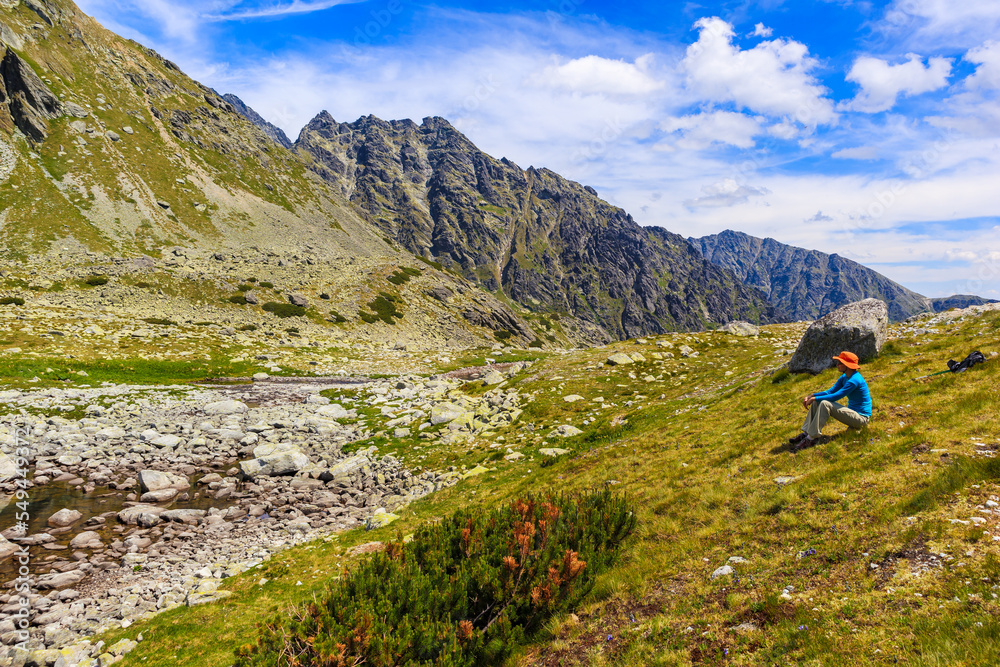 Woman tourist sitting on grass and looking at Hinczowa valley on sunny summer day, High Tatra Mountains, Slovakia