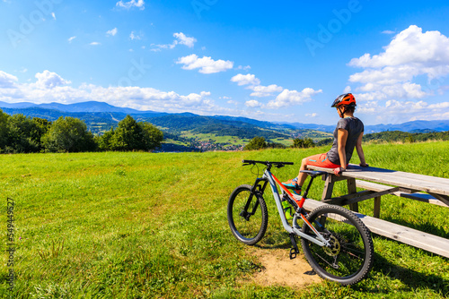 Woman mountain biker sitting on wooden table on green meadow in summer, Beskidy Mountains near Zywiec, Poland