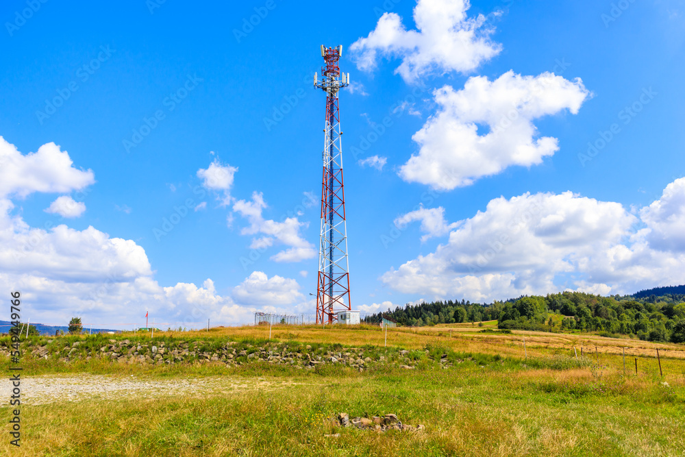 Cellphone tower on green meadow with flowers in Beskidy Mountains on sunny summer day near Zywiec, Poland