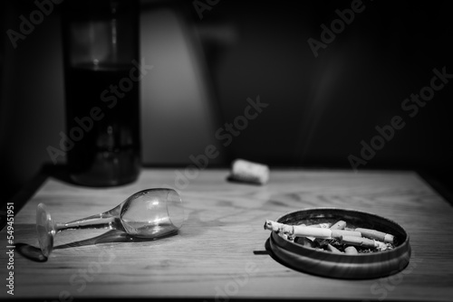 an overturned glass, spiled wine, and ashtray with cigarette butts 
 photo