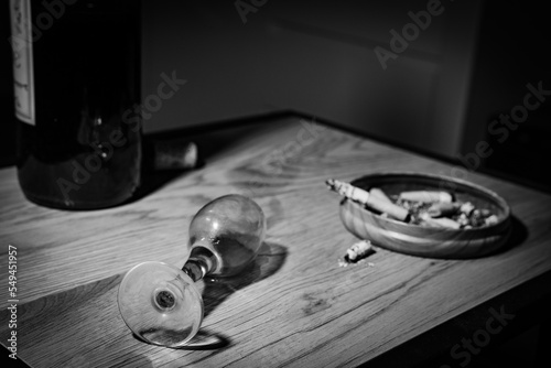 an overturned glass, spiled wine, and ashtray with cigarette butts in background
 photo