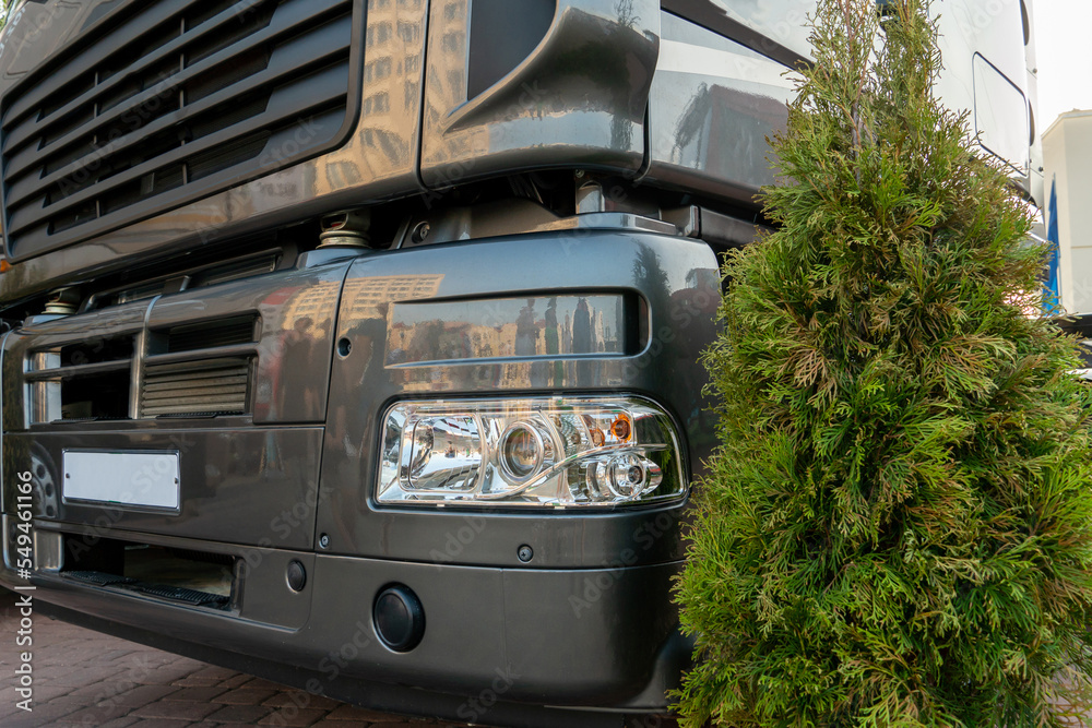 Obraz premium A big truck on the road. Modern new halogen headlights on a truck. Truck headlights. Square red headlight and reflector on the back of the hood. Car detail, close-up.