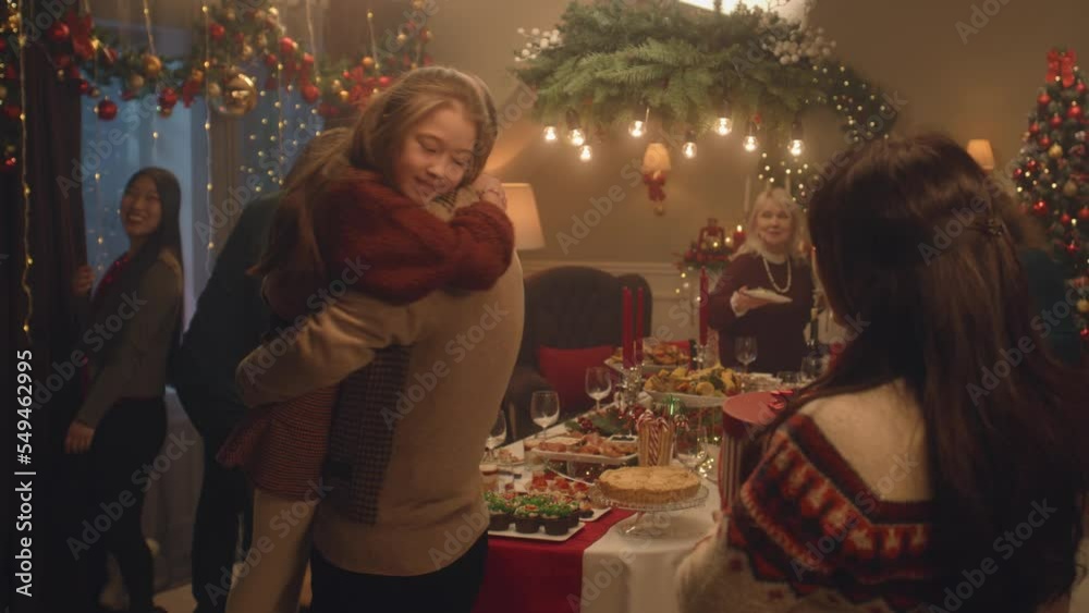 Happy diverse family arriving for dinner party celebrating Christmas or New Year. They hugging, talking, smiling, setting table with dishes. Family holidays and Christmas Eve. Decorations.