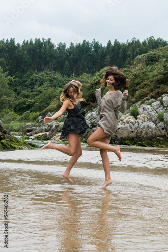 Two female friends playing around a river mouth on a beach in the cantabrian sea.