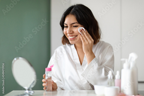Woman using micellar water and cotton pad for makeup removal photo