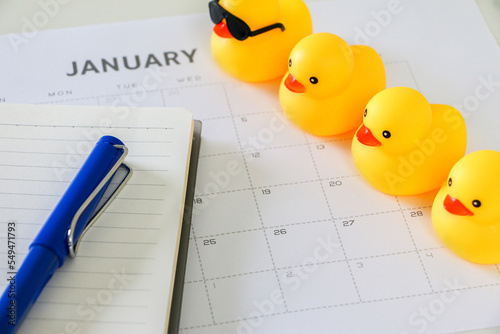 Foto Four yellow rubber ducks in a line on top of January calendar along with notebook and blue pen