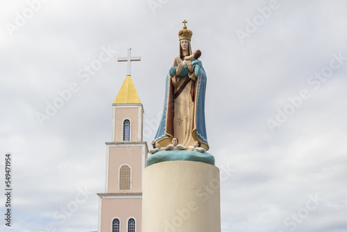 Imagem de Nossa senhora em primeiro plano e detalhe da Paróquia Nossa Senhora D'Abadia ao fundo, em um dia de céu nublado. Igreja na cidade de Anápolis em Goiás. photo