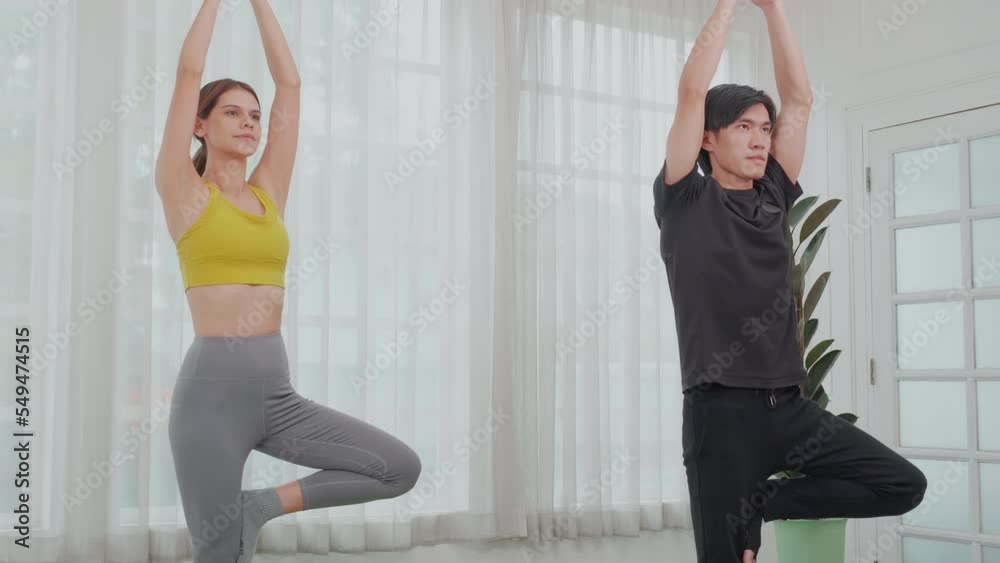 Young woman and asian man doing yoga with stretch muscles leg and hands at home, couple training practicing workout with yoga for bodycare, rehab with flexible of body, sport and health concept. Young woman and asian man doing yoga with stretch muscles leg and hands at home, couple training practicing workout with yoga for bodycare, rehab with flexible of body, sport and health concept.