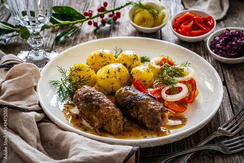 Wrapped pork in sauce served with boiled potatoes and vegetable salad on wooden table
