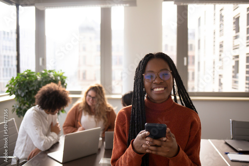 Black girl in foreground is taking a break in the office, using phone