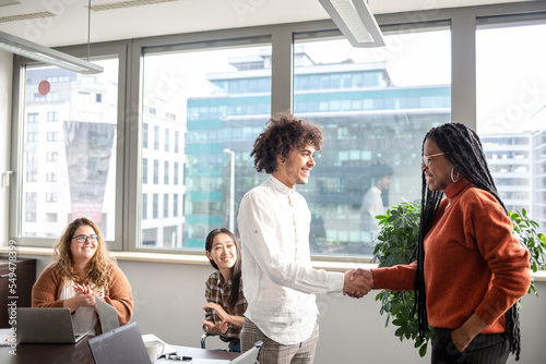 Four boys work in the office. A team leader shakes hands with an employee in congratulations