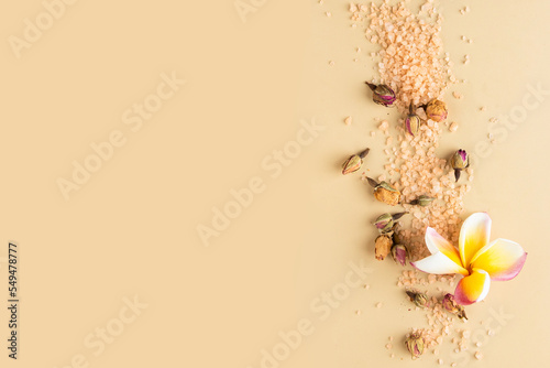 SPA flat lay composition, top view of scrab salt and frangipani flower  with roses on beige background for wellness treatment, relax and massage concept. photo