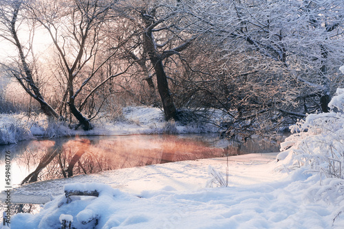 Tranquil winter river with snow covered trees. Christmas frosty landscape at sunrise or sunset.