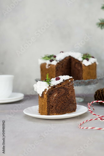 A piece of Christmas cake on plate on grey table with cup of tea and christmas cake on the glass stand.