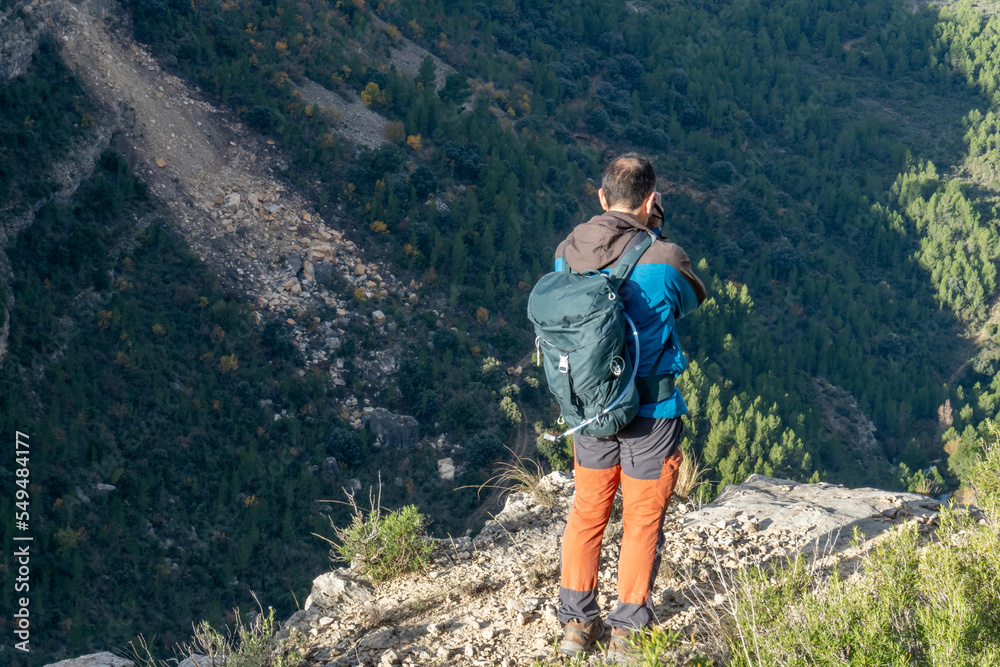 Obraz premium Rear view, standing man on a rock taking photos to the landscape