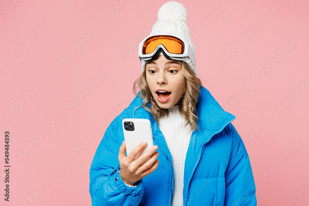 Snowboarder amazed woman wear blue suit goggles mask hat ski padded jacket hold use mobile cell phone isolated on plain pastel pink background. Winter extreme sport hobby weekend trip relax concept. Snowboarder amazed woman wear blue suit goggles mask hat ski padded jacket hold use mobile cell phone isolated on plain pastel pink background. Winter extreme sport hobby weekend trip relax concept.