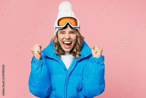 Snowboarder happy woman wear blue suit goggles mask hat ski padded jacket do winner gesture celebrate isolated on plain pastel pink background. Winter extreme sport hobby weekend trip relax concept