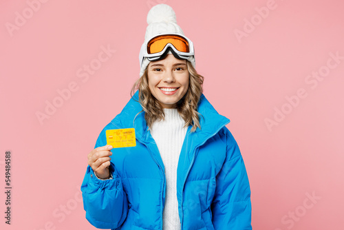 Snowboarder woman fun wear blue suit goggles mask hat ski padded jacket hold mock up of credit bank card isolated on plain pastel pink background Winter extreme sport hobby weekend trip relax concept