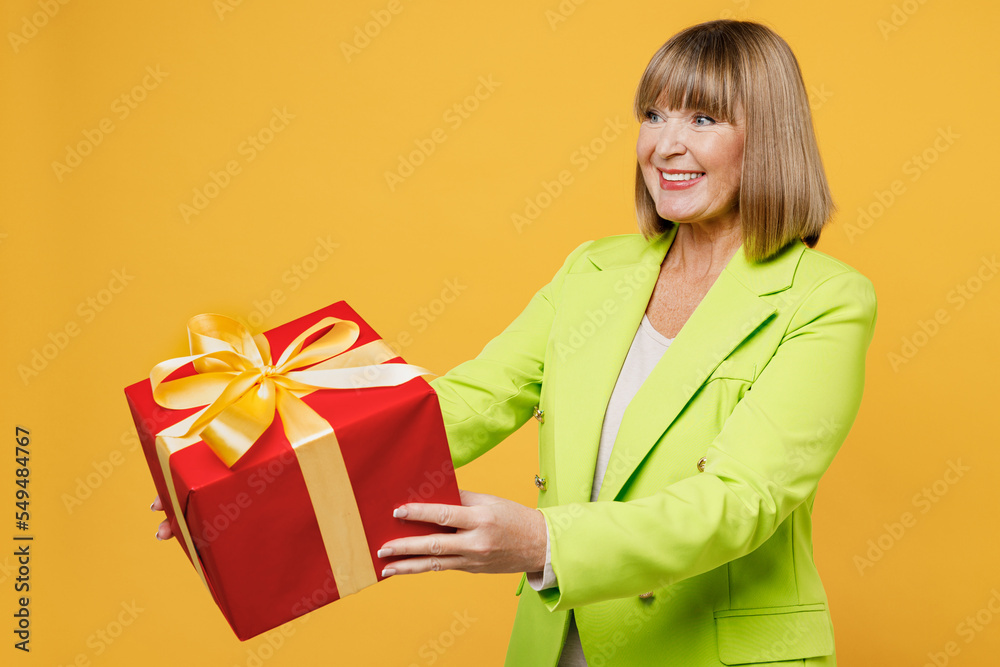 Side view elderly happy woman 50s year old in green jacket white t-shirt hold give gift certificate coupon voucher card for store isolated on plain yellow background studio. People lifestyle concept Side view elderly happy woman 50s year old in green jacket white t-shirt hold give gift certificate coupon voucher card for store isolated on plain yellow background studio. People lifestyle concept