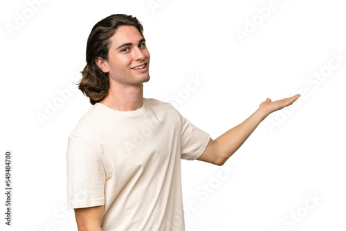 Young caucasian man isolated on green chroma background extending hands to the side for inviting to come
