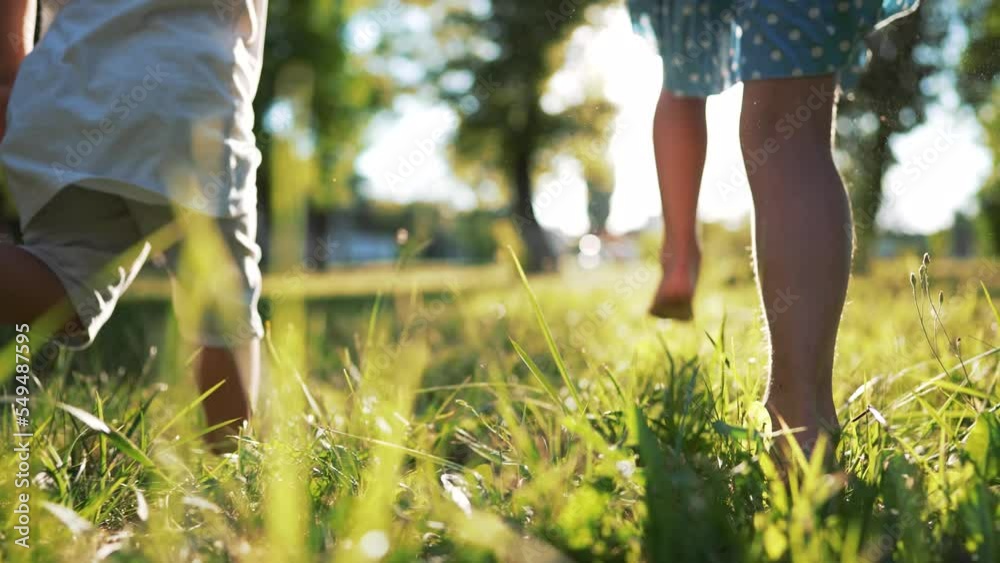 Happy family.Toddlers run barefoot on the green grass in park at sunset.Active running in nature.Summer picnic healthy lifestyle.Legs of children in park on grass.Brother and sister outdoors in summer