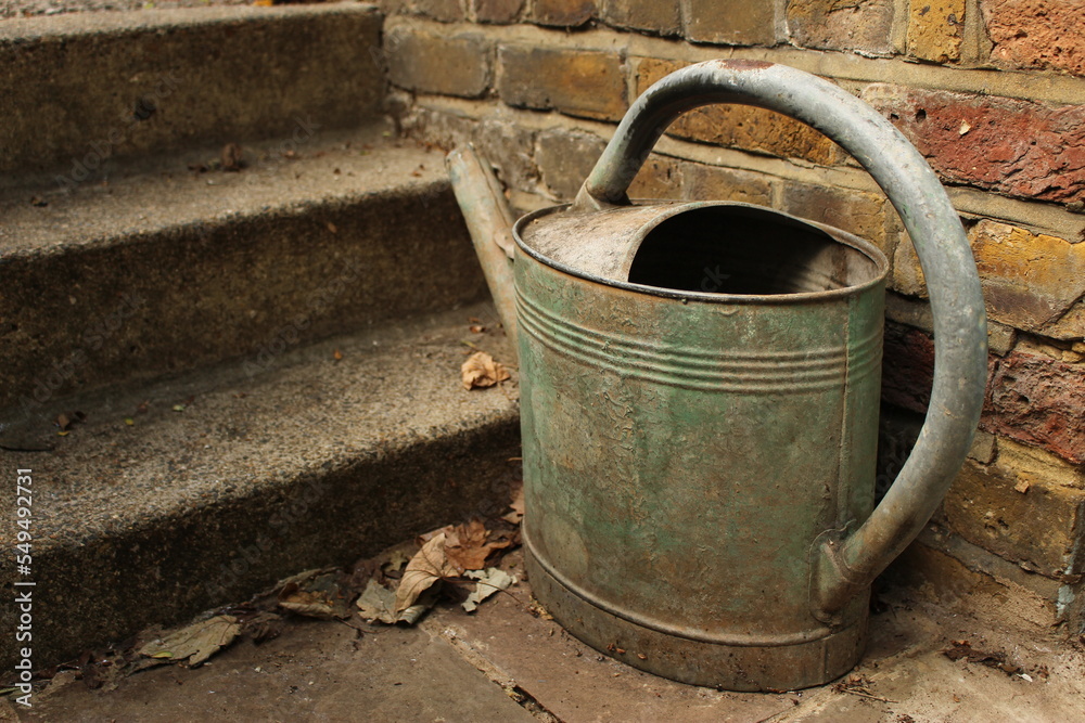 Old watering can at the base of stone steps. Autumnal fall background wallpaper backdrop concept Old watering can at the base of stone steps. Autumnal fall background wallpaper backdrop concept