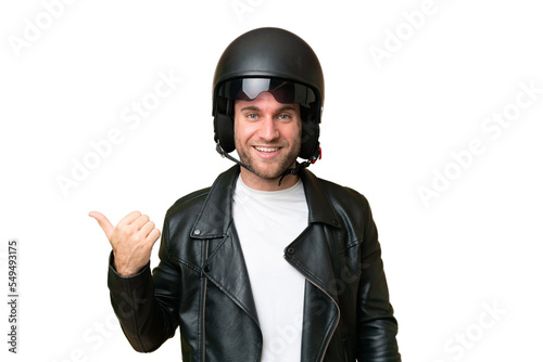 Young caucasian man with a motorcycle helmet isolated on green chroma background pointing to the side to present a product