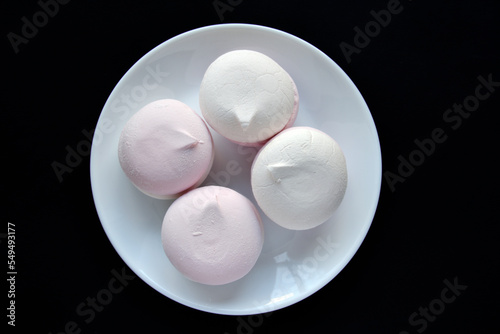 Pink and white marshmallows on a white plate on a black background. Delicious sweet snack on a plate. Marshmallow close-up.