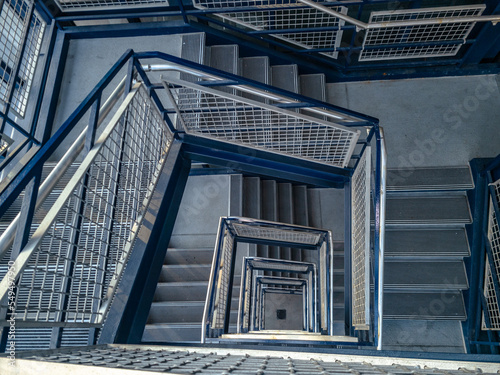 Stairwell in a parking garage. The steps in the stairwell are made of concrete and the hand railings are metallic and painted blue. Located at the big blue deck at the Detroit Metro Airport in Romulus
