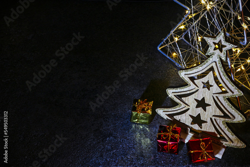 Low key wooden christmas tree with presents and with lights in the background