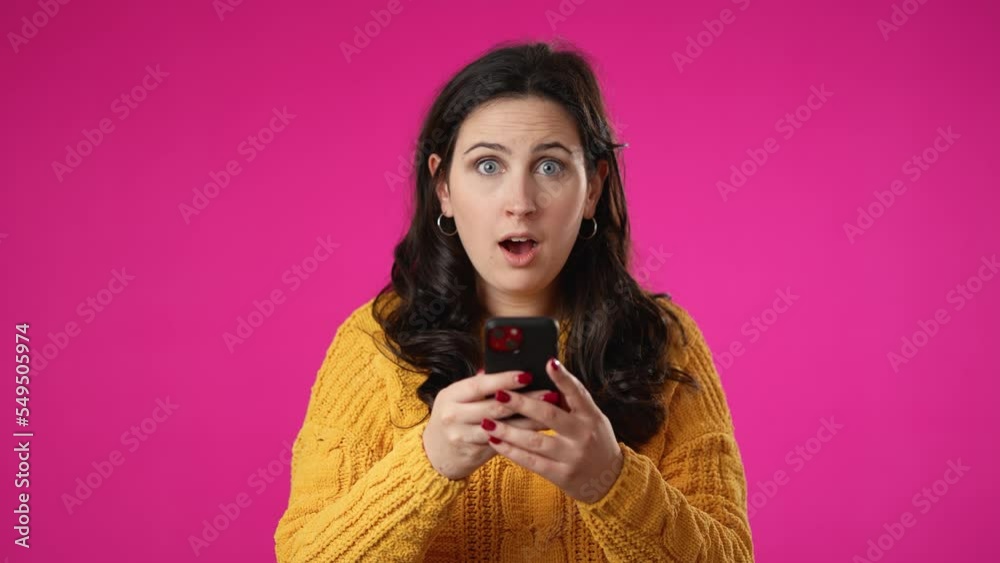 Portrait of happy smiling young pretty woman 20s in sweater shopping on mobile phone point with finger give thumbs up isolated on pink background studio. Portrait of happy smiling young pretty woman 20s in sweater shopping on mobile phone point with finger give thumbs up isolated on pink background studio.