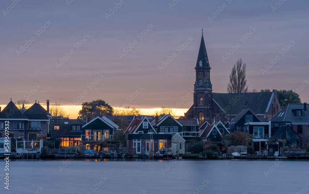 Church in the town of Zaandijk by sunset with river Zaan in the foreground seen from Zaandam