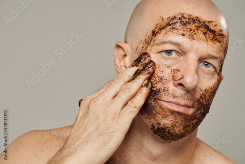 Handsome mature man rubbing face with antioxidant coffee grounds scrub horizontal portrait photo