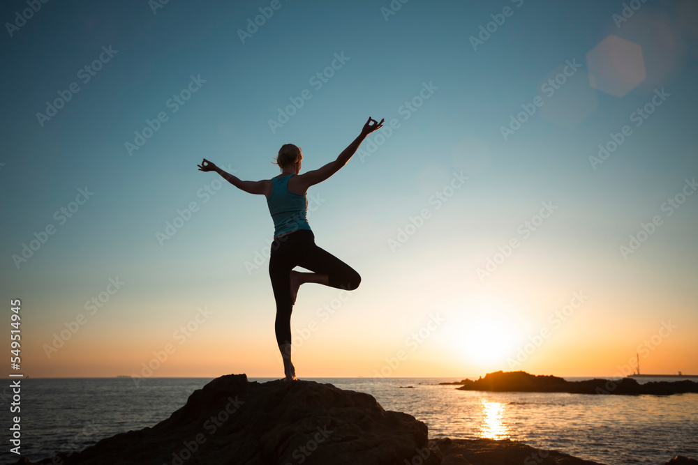 A woman doing yoga on the beach during sunset.