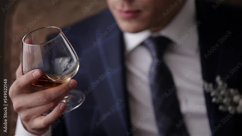 A cute guy is sitting on a chair with a glass of wine in his hand. Shooting in close-up A cute guy is sitting on a chair with a glass of wine in his hand. Shooting in close-up